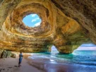 Praia Benagil Cave no Algarve com luz solar entrando pelo teto circular, iluminando a areia dourada e águas turquesa cristalinas.