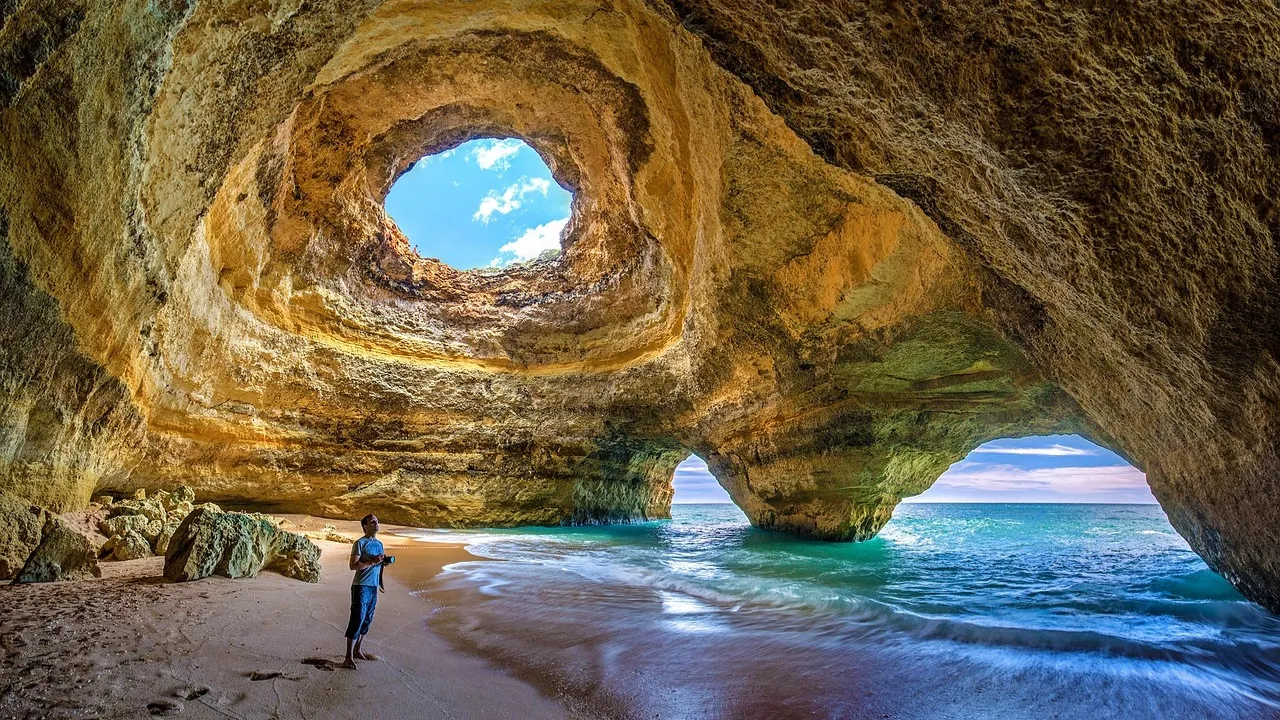 Praia Benagil Cave no Algarve com luz solar entrando pelo teto circular, iluminando a areia dourada e águas turquesa cristalinas.